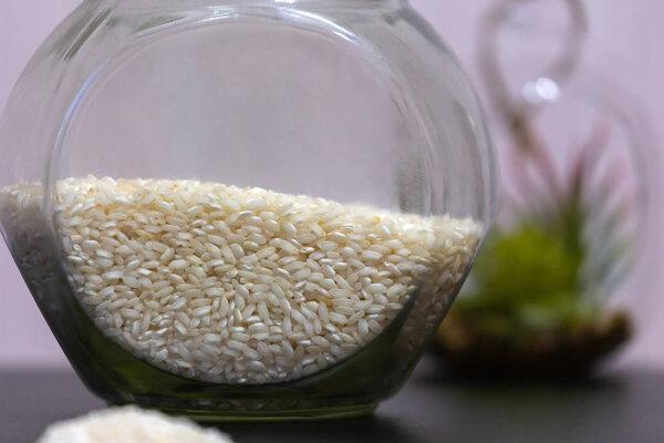 Healthy eating rice groats in a glass jar standing on a table with a green plant on the background