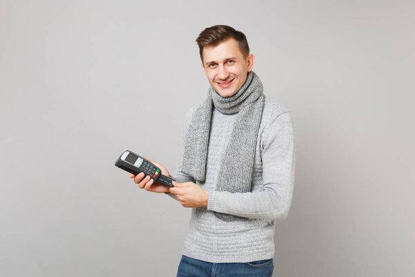 Smiling man holding wireless modern bank payment terminal to process, acquire credit card payments isolated on grey background. Healthy fashion lifestyle, people sincere emotions, cold season concept