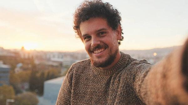 Smiling guy stands on the balcony at dawn, takes selfie on smartphone
