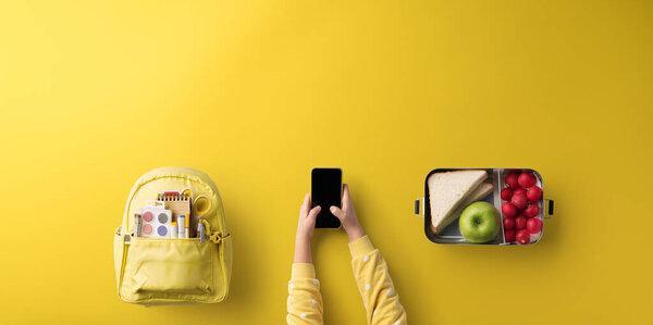 Flat lay top view of child hands with smartphone, healthy snack and back to school concept.