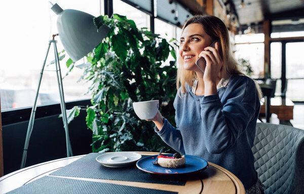 Smiling girl having phone conversation, while sitting at cafe