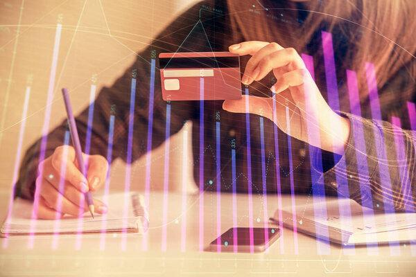 Double exposure of woman on-line shopping holding a credit card and financial graph drawing. Stock market E-commerce concept.