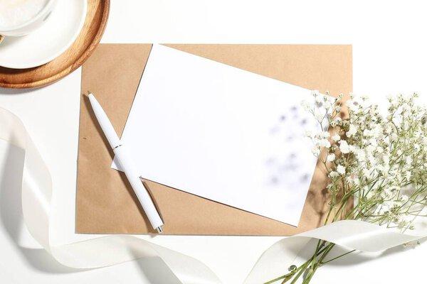 Blank card, envelope, pen, ribbon and beautiful flowers on white background, flat lay