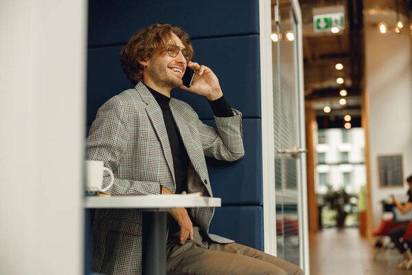 Handsome businessman talking by mobile phone with client while sitting in coworking 