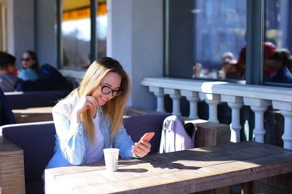 Girl using smartphone and sitting at cafe with cup of tea.