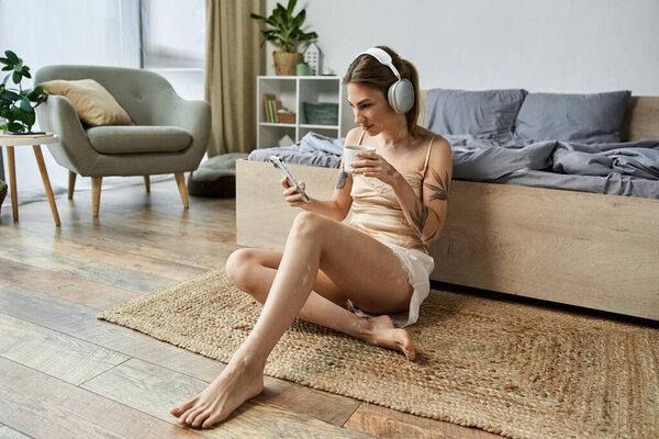 A young woman with vitiligo and a tattoo relaxes in her cozy bedroom, listening to music and enjoying a cup of coffee.
