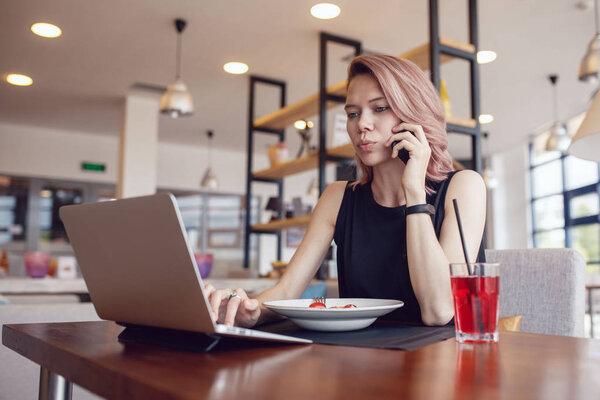 Business woman eats at a cafe and uses a smartphone and laptop.