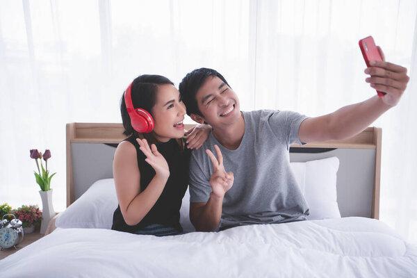 Asian couple lovers lying on their play mobile phones and selfie on bed at home