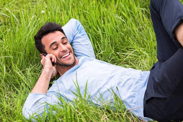 Surprised and happy business man talking on the telephone lying on the green grass