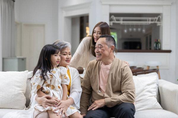 家人在舒适的客厅里度过快乐的时光，有三代人在场。祖父母对孙女笑着，而母亲则享受着温暖的空气.