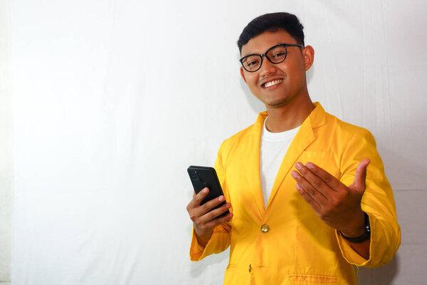 身穿黄色夹克、戴眼镜、手持智能手机的印尼年轻人