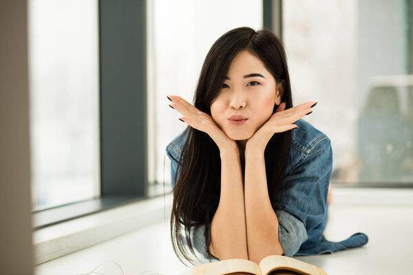 asian woman reading a book next to big windows