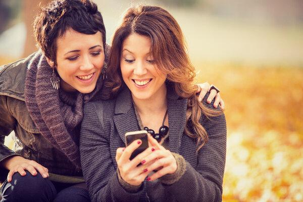 couple of girl Friends having fun with phone at the park