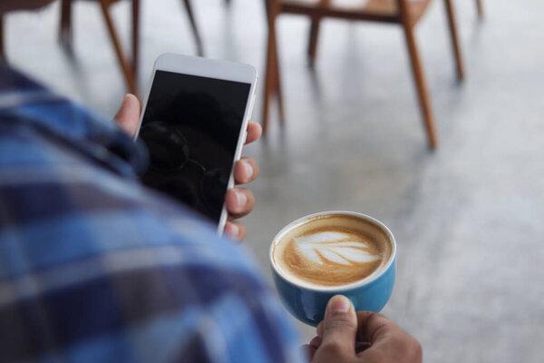 Close up of Asian man holding a cup of coffee and mobile phone. Technology and morning routine concept