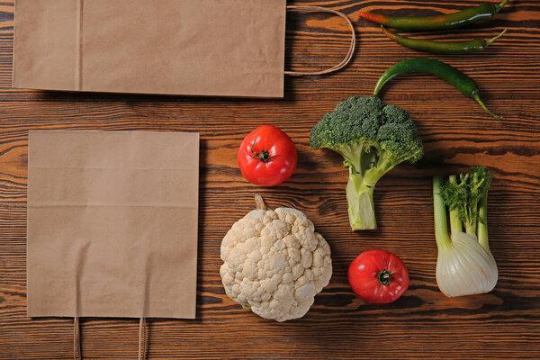 Paper eco bags with fresh vegetables on wooden background