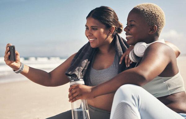 Our fellow yogis will love this one. two sporty young women taking a selfie while exercising at the beach