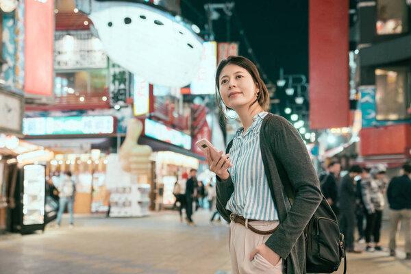young lady backpacker standing on the temming street in tsutenkaku. fish balloon hanging in the dark blue sky in city in osaka. woman urban night lifestyle.