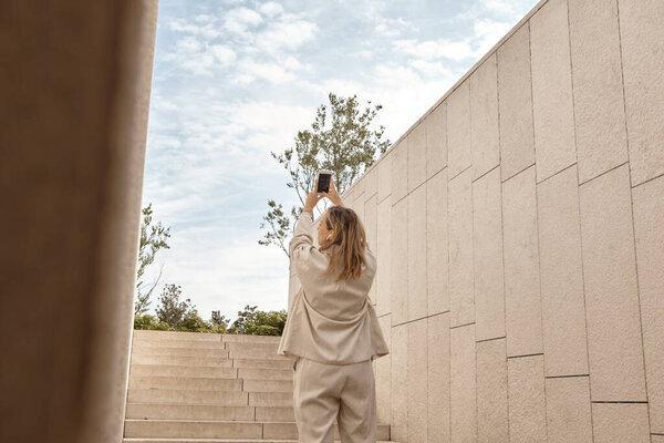 A woman stands on the stairs and takes pictures of the sky on her mobile phone. Daily use of modern technologies