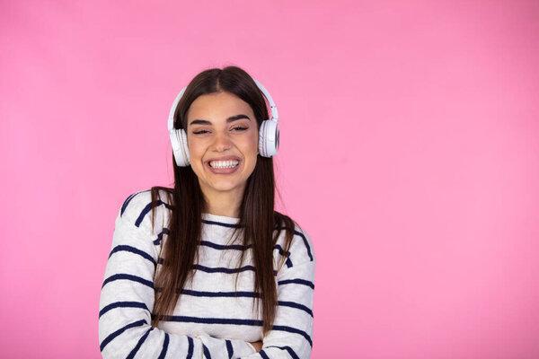 Cropped shot of a beautiful young woman wearing headphones against a pink background. Smiling young woman listening to music with headphones  against isolated pink background