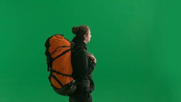 Half-turned view of a male traveler with a large hiking backpack on his back. The man is standing full-length and enjoying the view. Hiker in studio on green screen