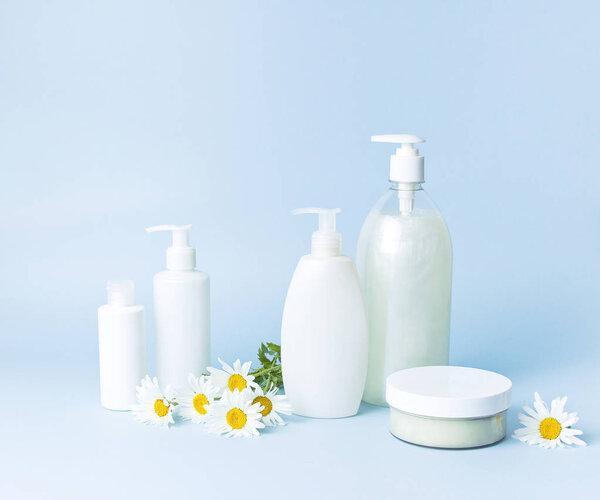 Cosmetic bottle containers with chamomile flowers on a blue minimalistic background flat lay. Blank label for branding mock-up. Natural beauty product concept