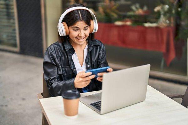 Young beautiful hispanic woman playing video game sitting on table at coffee shop terrace