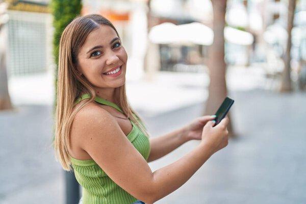 年轻美丽的惊慌失措的女人在街上用智能手机充满自信地微笑