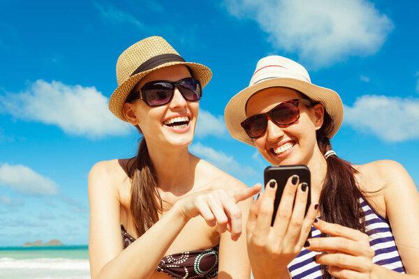Happy beautiful women using mobile smart phone at the beach