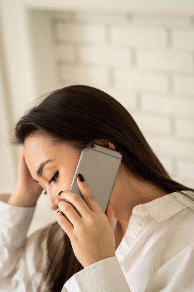 一个年轻的黑发女子坐在那里，耳朵上拿着电话。一个漂亮的黑头发姑娘正在和她的朋友通电话。高质量的照片