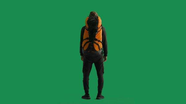Back view of a male traveler with a large hiking backpack on his back. The man is standing full-length and enjoying the view. Hiker in studio on green screen