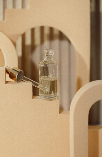 Glass dropper bottle with pipette on abstract trendy podium for cosmetics product presentation in nude colors. Showcase with face serum or skin essence. Natural skincare concept