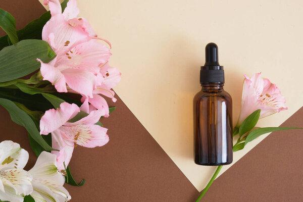 Amber glass bottle with pipette on a beige brown background with lily flowers. copy space. Natural cosmetic, skin care concept