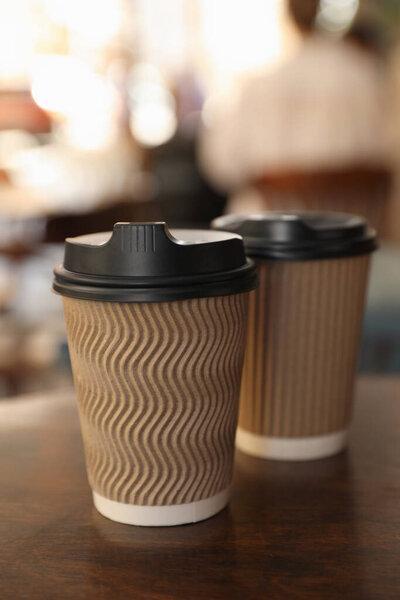 Cardboard takeaway coffee cups with plastic lids on wooden table in city