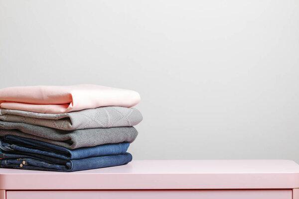 On a pink table is a stack of folded clothes. Gray background. Close-up
