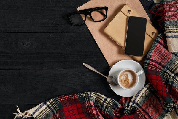 Above view of Smart phone with notebook and cup of latte coffee on black wooden background.