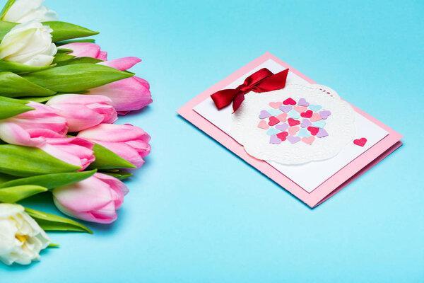Bouquet of tulips near greeting card on blue surface