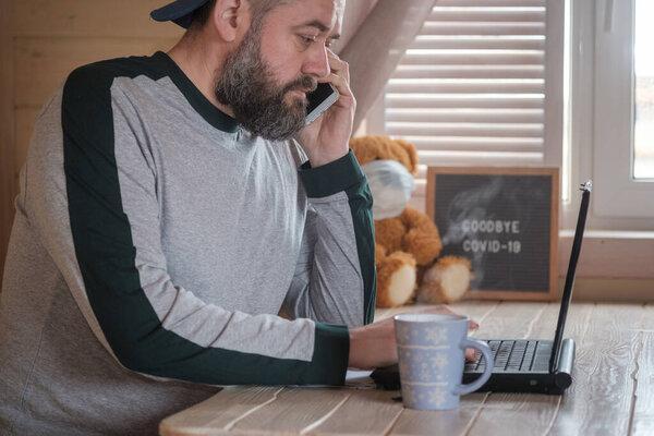 a brutal man with a beard is sitting at home at a table in front of a laptop screen. concept of remote work during quarantine and pandemic covid-19. online work from home