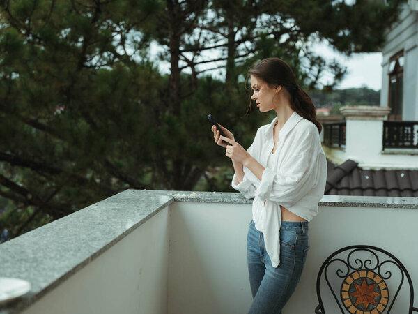 女人在房子的阳台上，带着电话的美丽微笑在一天的休假，美丽的自然景观在山上，生活方式在酒店度假。高质量的照片
