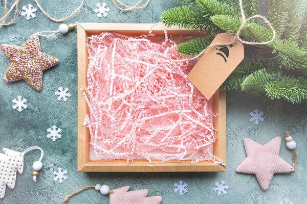 Empty gift box with pink paper filling on green background with Christmas decor.