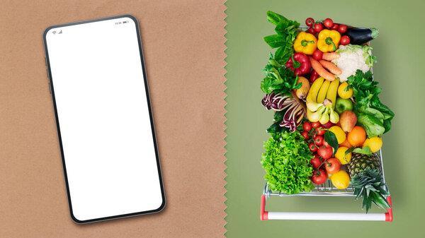 Supermarket shopping cart full of groceries and smartphone with blank screen, online grocery shopping concept