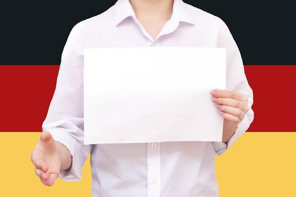 man with a white sheet of paper in his hands, for your text, mockup. Against the background of the flag of Germany. Unknown person. He reaches out for agreement.