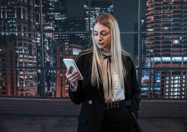 Young caucasian business woman in black suit checks email on smartphone cellphone at office. Lifestyle