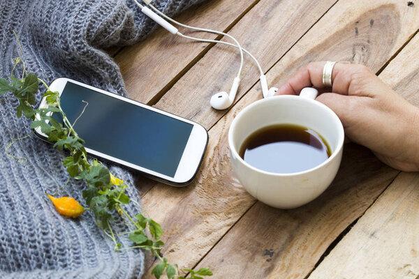 hand of woman holding hot coffee espresso with mobile phone ,knitting wool scarf of lifestyle woman relax in winter season decoration on background wooden