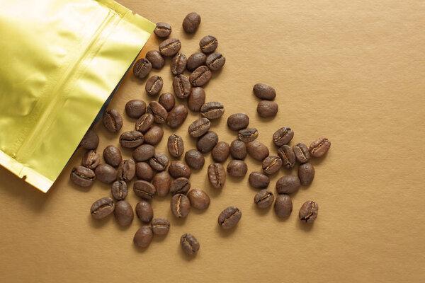 Gold foil bag with coffee beans on golden background. Packaging template mockup. Aluminium package for tea, flatlay.