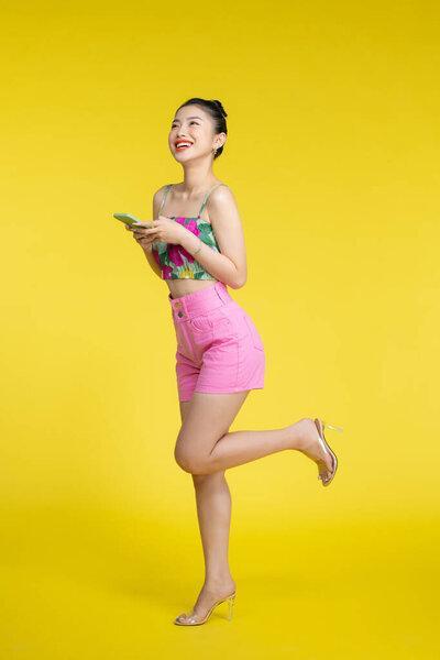 一个面带微笑的年轻亚洲女人用黄色背景的手机的肖像