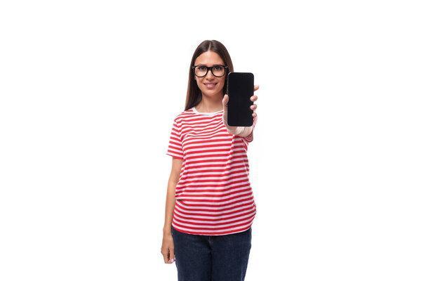 portrait of a young pretty european brunette woman dressed in a summer striped t-shirt with a smartphone in her hand on a white background.