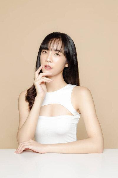 年轻美丽的亚洲女人，有刘海和新鲜光滑的皮肤。漂亮的女模特,有着自然的妆容,一双闪亮的眼睛,衬托着米色的背景.面部护理、面部治疗、美容、美容和温泉.