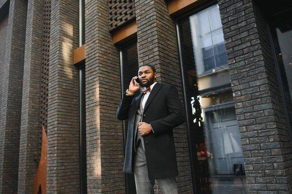 Business communications. Happy young African man in formal wear talking on the mobile phone and smiling while standing outdoors