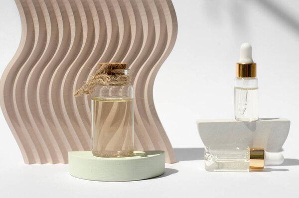 A bottle of essential oil on a podium with harsh shadows. Natural oils in transparent bottles on a white background with geometric shapes.