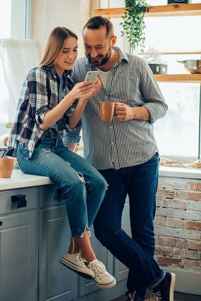 Cheerful man and woman in the kitchen smiling and looking at smartphone